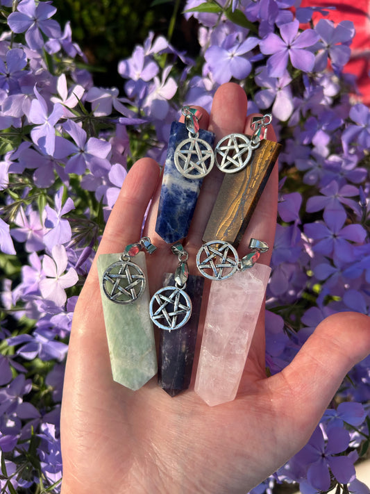 Hand holding assorted crystal pentacle pendants with purple flowers background