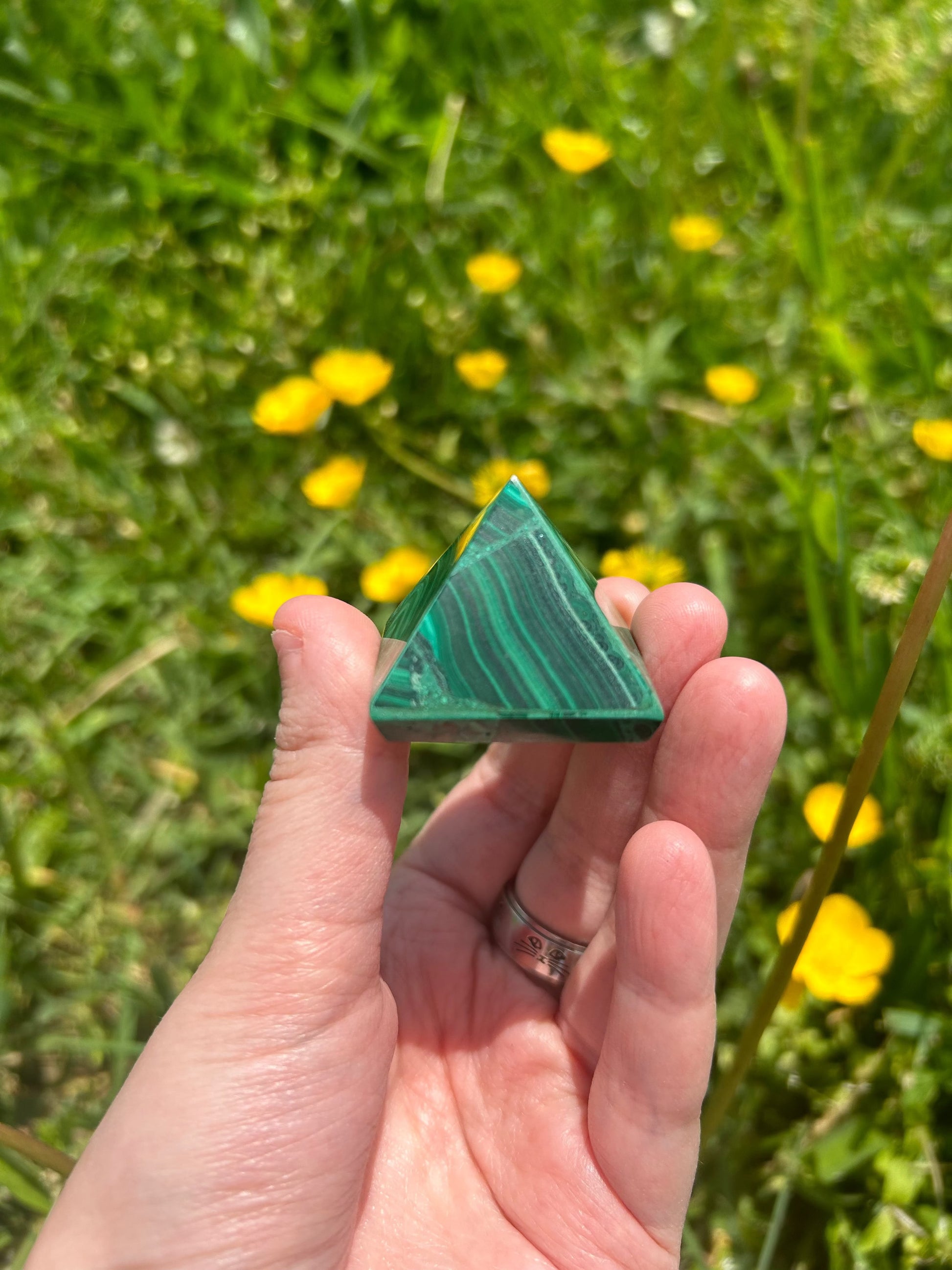 hand holding green Malachite Pyramid crystal with yellow flowers and grass background