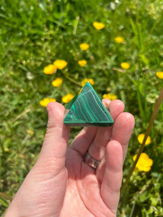 hand holding green Malachite Pyramid crystal with yellow flowers and grass background