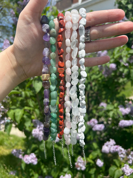 Hand holding colorful crystal nugget chokers in outdoor natural light with green foliage background
