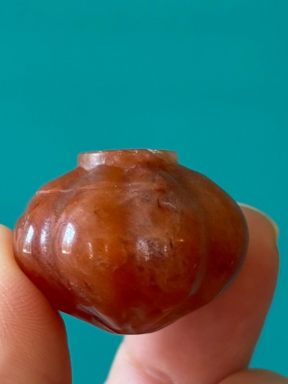 Hand holding small orange calcite Halloween pumpkin carving against teal background