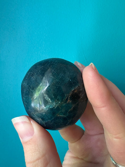 Smooth blue apatite pebble palm stone held against turquoise background