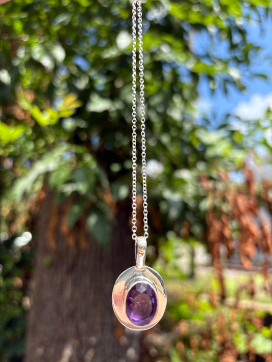 Amethyst pendant sterling silver necklace with purple gemstone on chain against natural outdoor background