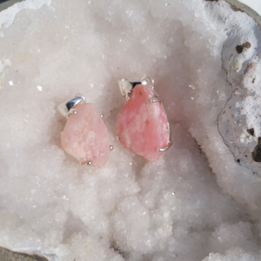 Raw pink opal pendant with silver setting on white crystal background