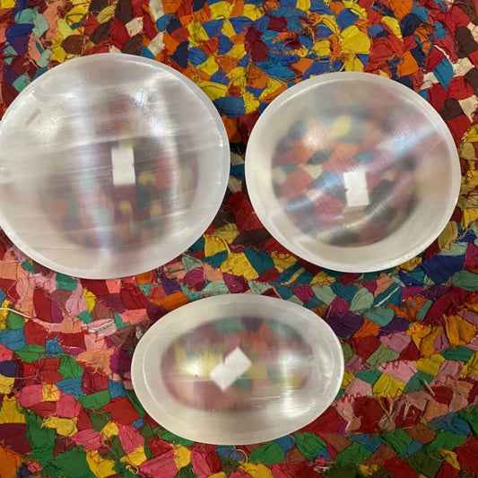Three smooth translucent selenite bowls with varying shapes on a colorful woven fabric background