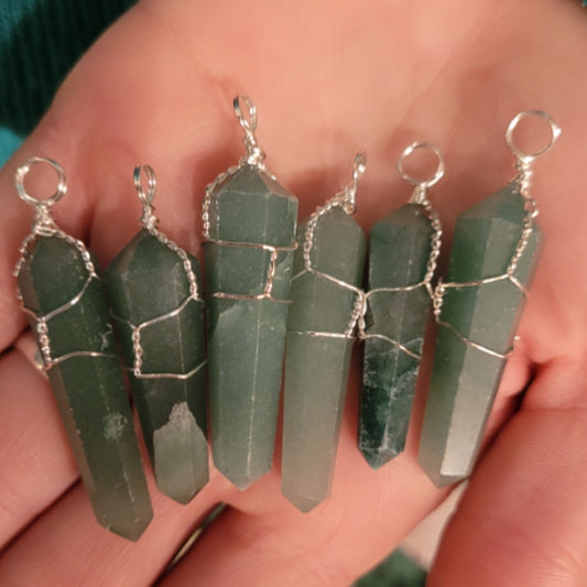 Hand holding multiple green aventurine wire wrapped pendants with silver loops