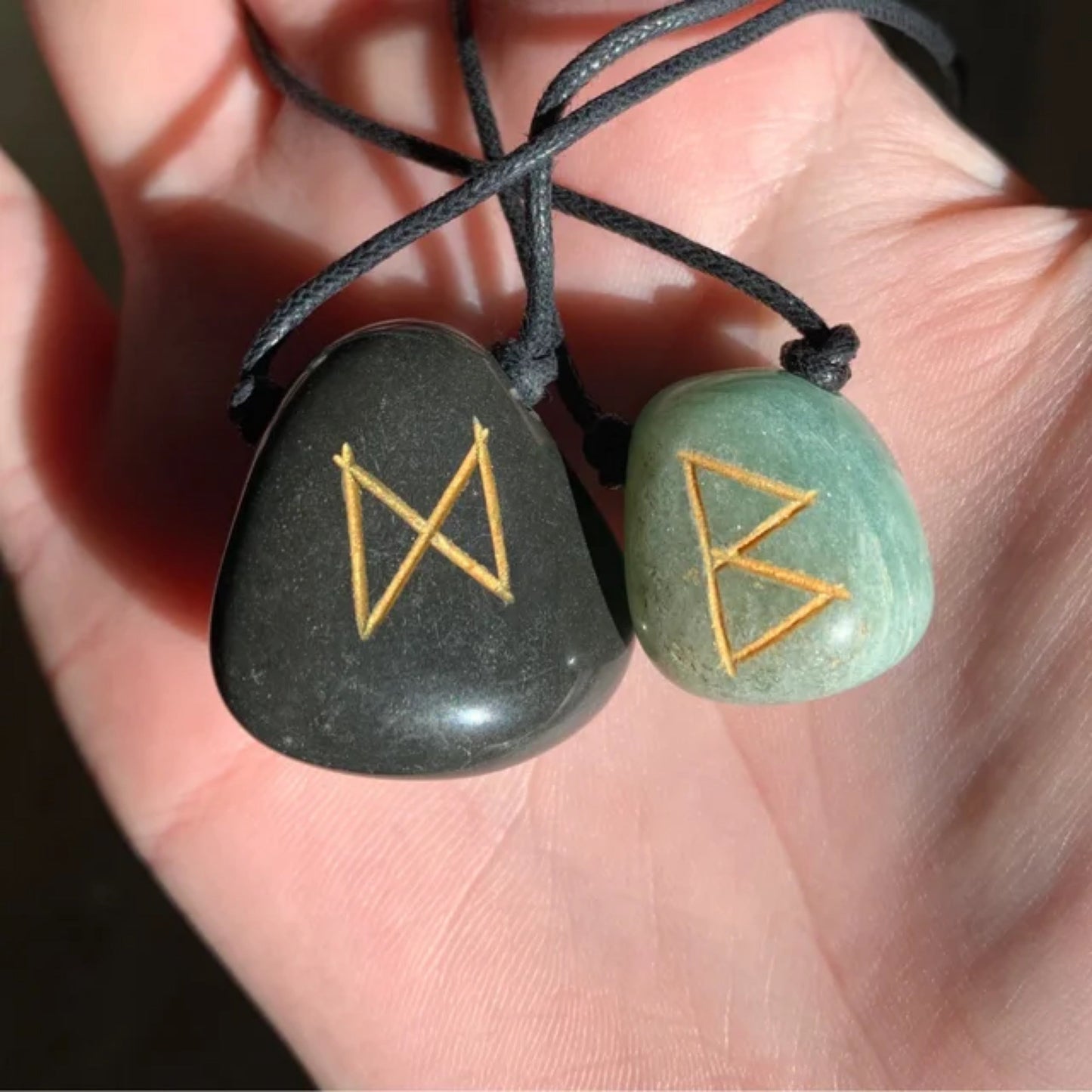 Two agate rune necklaces with hand-carved golden symbols on black and green stones held in a hand