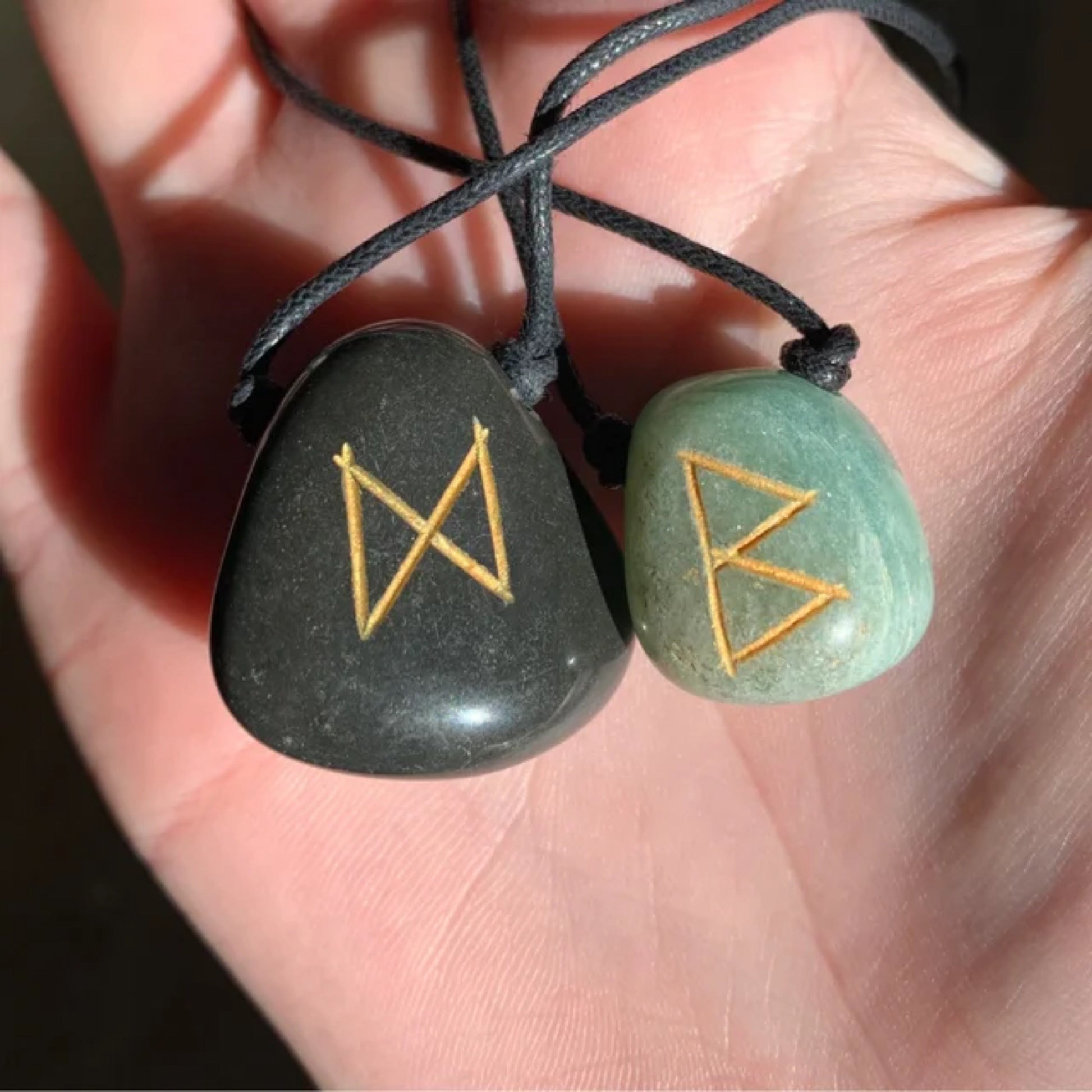 Two agate rune necklaces with hand-carved golden symbols on black and green stones held in a hand