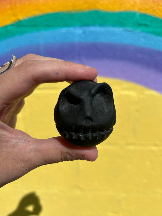 Hand holding a smooth black obsidian Jack Skellington skull carving with a colorful rainbow background
