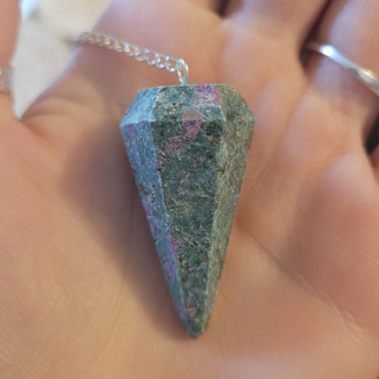 Hand holding a multi-colored crystal pendulum with a silver chain for divination and energy work