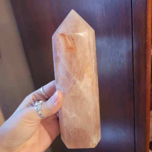 Hand holding a polished hematite quartz tower with natural red and orange inclusions against a wooden background