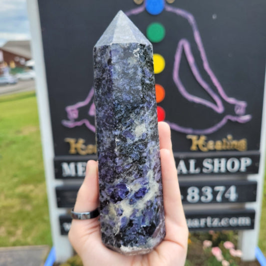 Hand holding polished Iolite crystal point embedded in Black Mica background outdoors