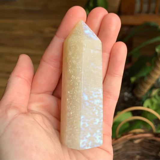 Hand holding a polished tower-shaped blue moonstone crystal with natural iridescent glow