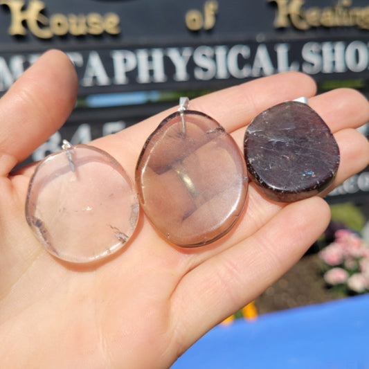 Hand holding three smokey quartz slice pendants with silver bails against an outdoor background