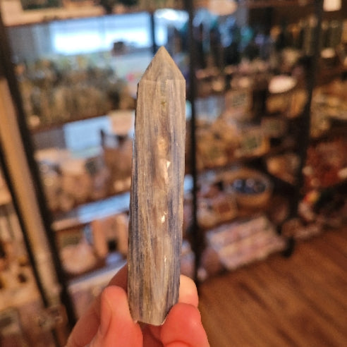 Hand holding a polished blue kyanite tower crystal with natural blade-like formations in a blurred shop background