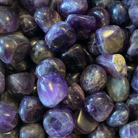 Close-up of polished dark purple Amethyst tumble gemstones with smooth surfaces and natural color variations