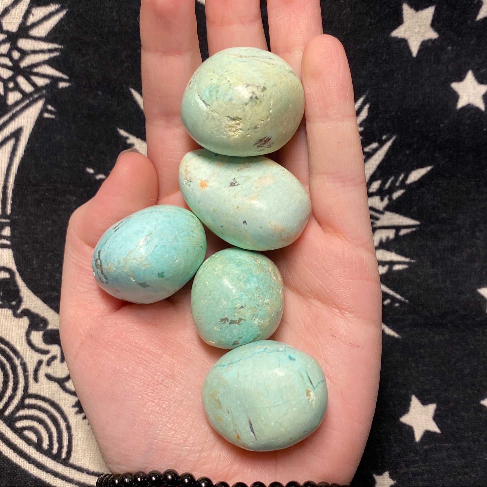 Hand holding Peruvian turquoise tumbles on a black and white star-patterned background