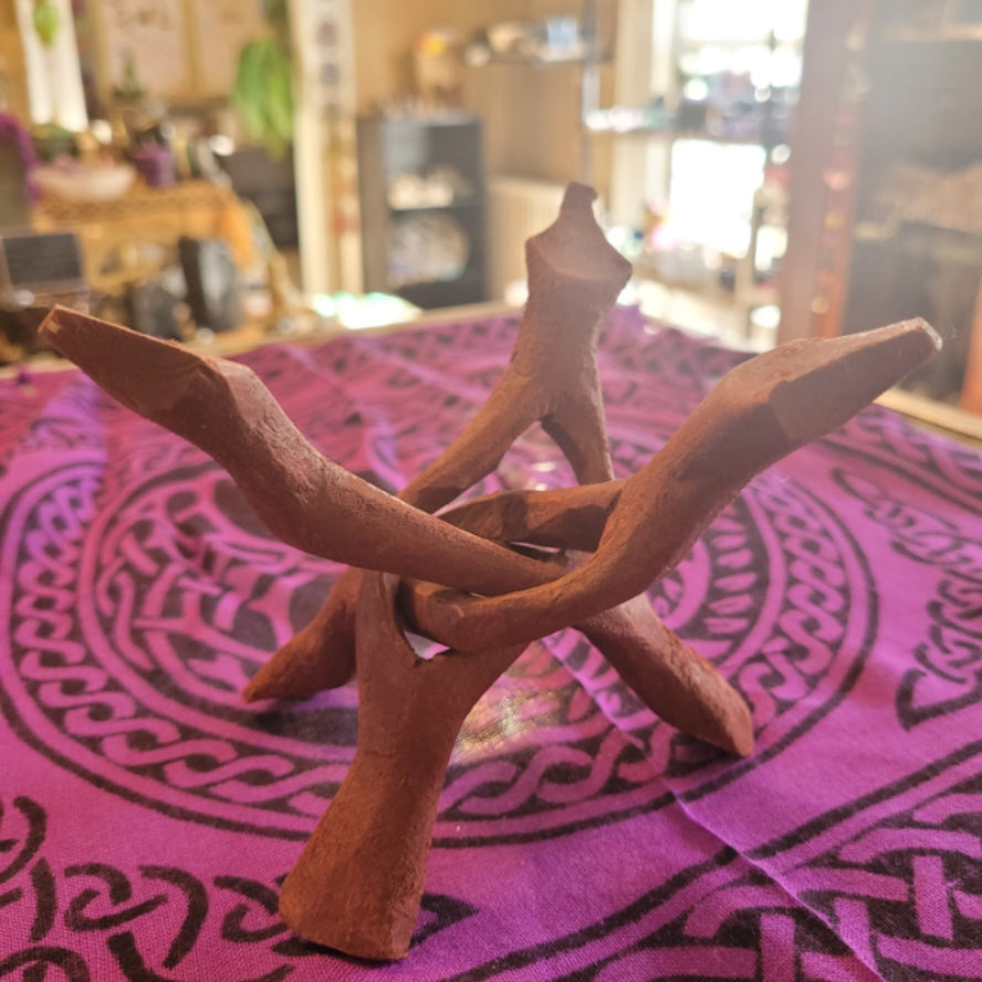 Red intertwined wooden stand designed to hold abalone shells on a patterned cloth background