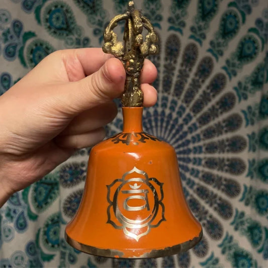 Orange Chakra Bell with gold detailing held against a patterned background