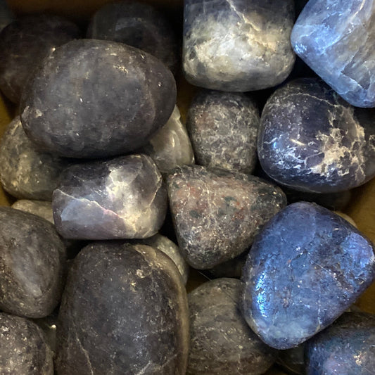 Pile of polished deep blue iolite tumbles with smooth surfaces and natural variations