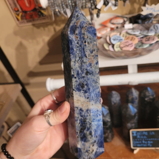 Hand holding a polished blue Sodalite Obelisk Tower with other similar towers displayed in the background