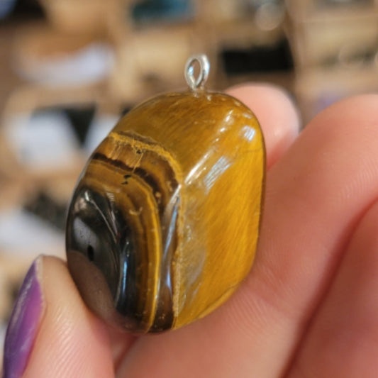 Close-up of a polished tiger eye pendant held between fingers