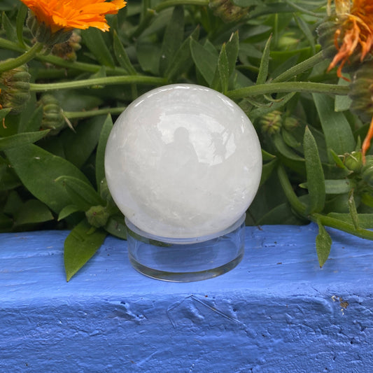 Clear quartz sphere on a clear stand with green foliage and orange flowers background
