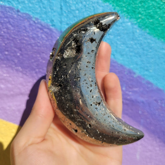 Hand holding a polished pyrite crescent moon stone against a colorful purple and blue background