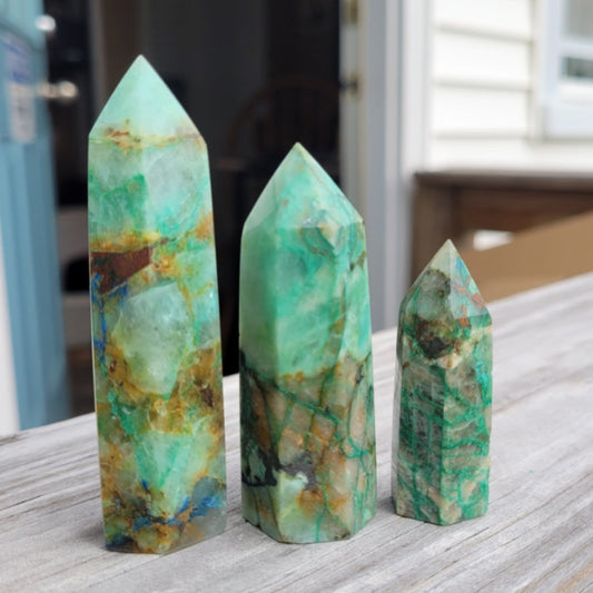 Three handcrafted Chrysocolla towers of varying sizes with blue-green hues on a wooden surface