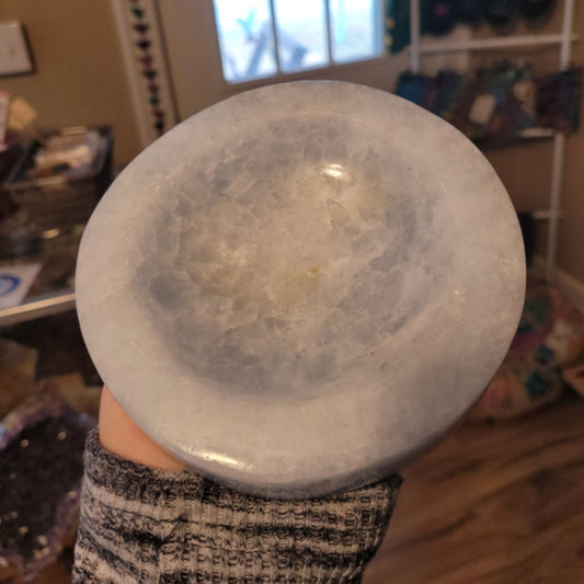 Blue calcite bowl held in hand showing smooth polished surface and translucent light blue hues.