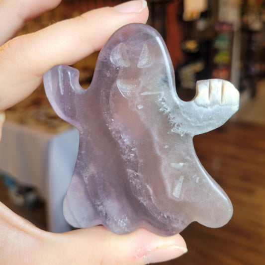 Hand holding a carved fluorite ghost figurine with a translucent purple hue and white crystal highlights