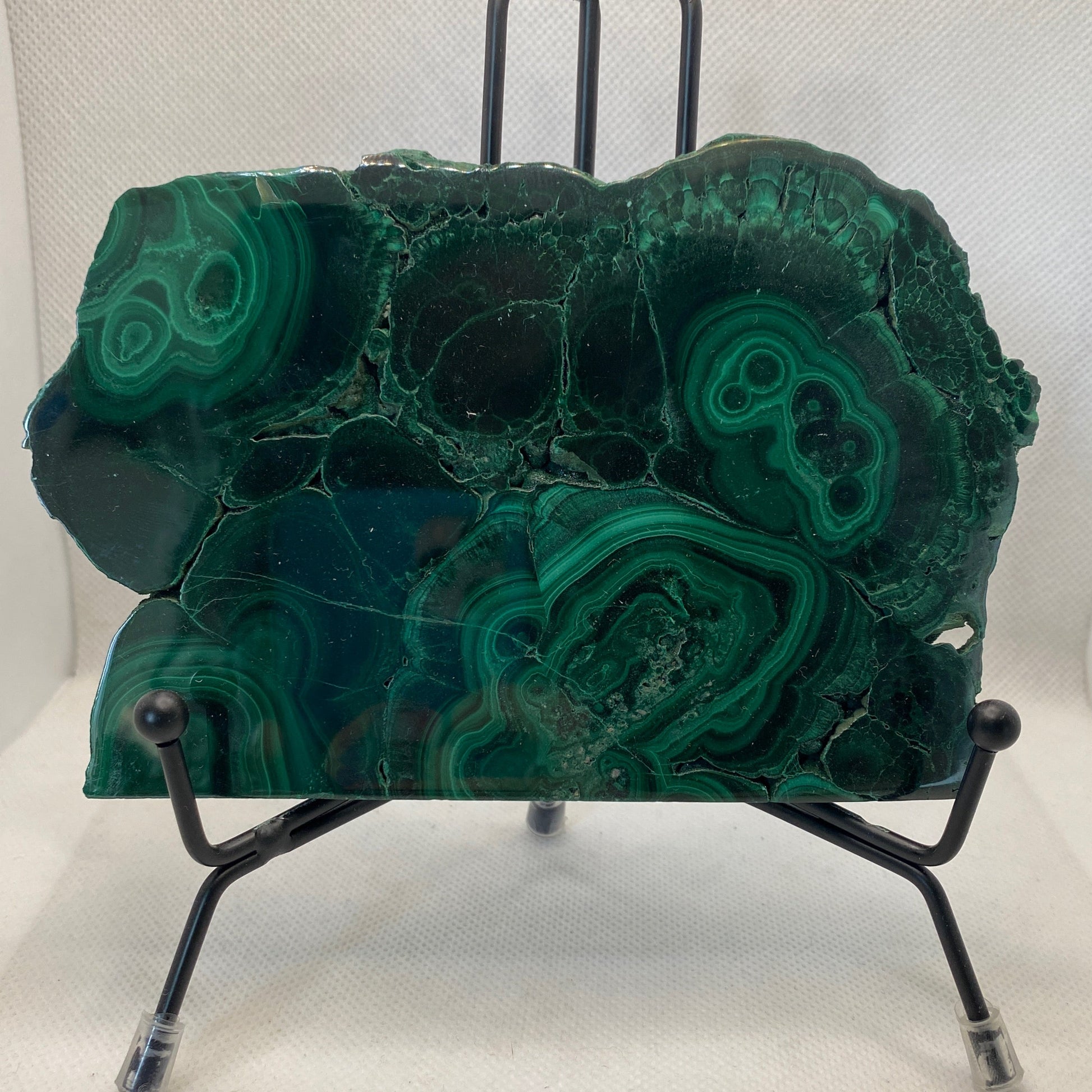 polished malachite slab with vibrant green hues and distinctive banding on a black metal stand