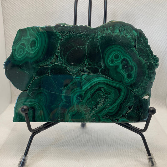 polished malachite slab with vibrant green hues and distinctive banding on a black metal stand