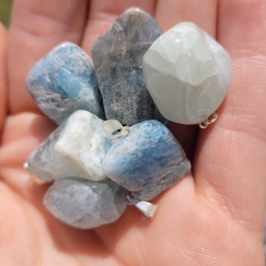 Hand holding genuine aquamarine pendants showcasing calming blue and white hues for mental clarity and inner peace