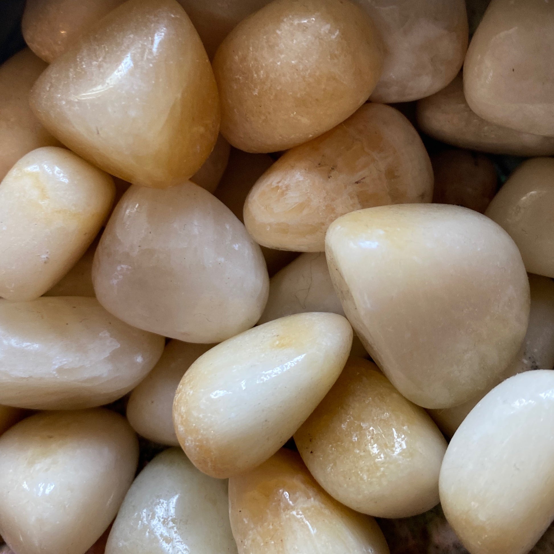 Close-up of polished yellow calcite tumble stones with smooth, glossy surfaces and warm, sunny hues