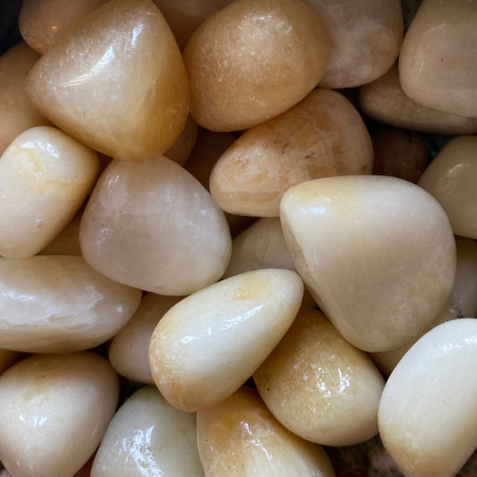 Close-up of polished yellow calcite tumble stones with smooth, glossy surfaces and warm, sunny hues