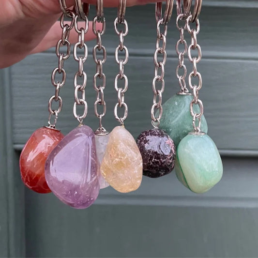 Set of colorful crystal keychains with silver chains and mushroom charms hanging against a gray background