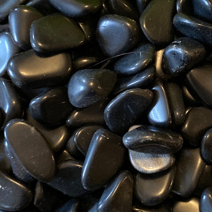Close-up of smooth black obsidian tumble stones with a glossy surface for grounding and healing practices