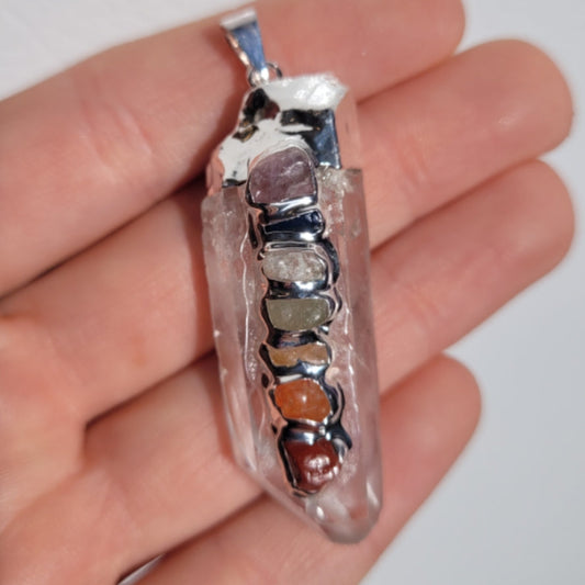 Clear quartz rough chakra pendant with seven colorful chakra stones held in hand