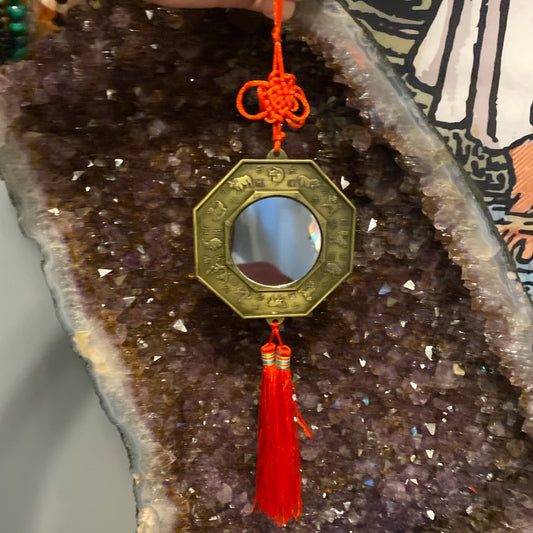 Feng Shui Mirror with octagonal brass frame and red tassel hanging on amethyst crystal background