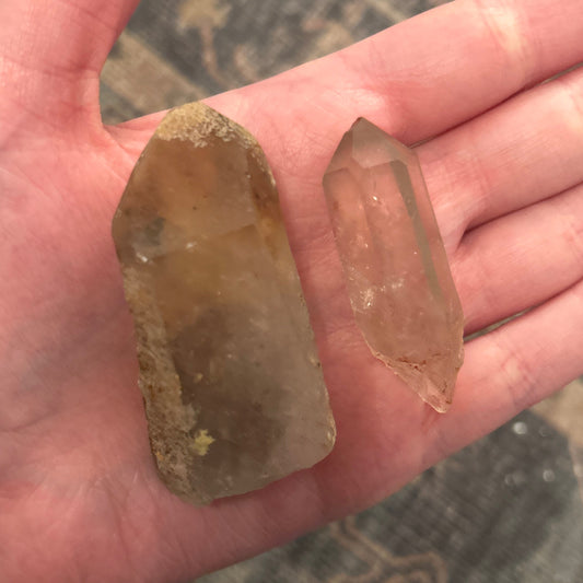 Two smokey quartz crystals with visible natural inclusions held in a hand against a blurred background