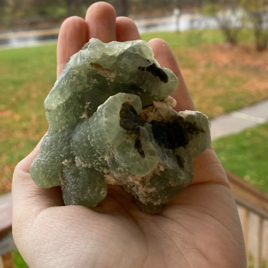 Hand holding raw Prehnite stone with Epidote inclusions outdoors