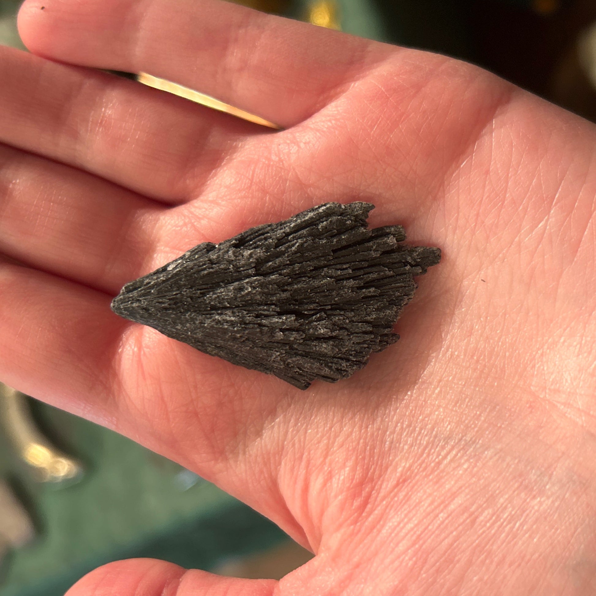 Raw black kyanite stone held in hand showing its natural layered texture and dark color
