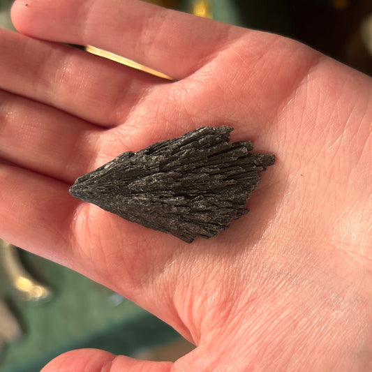 Raw black kyanite stone held in hand showing its natural layered texture and dark color