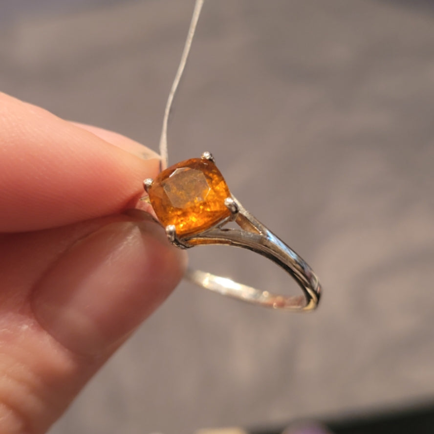 Silver ring with vibrant orange kyanite gemstone held between fingers