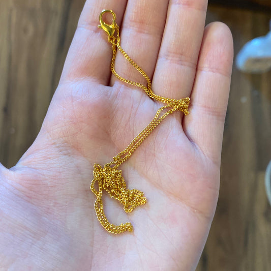 Close-up of a delicate gold chain necklace held in a person's hand