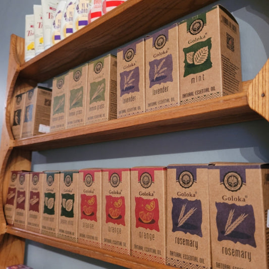 Various Goloka essential oils in cardboard packaging displayed on wooden shelves including lavender, mint, orange, and rosemary scents