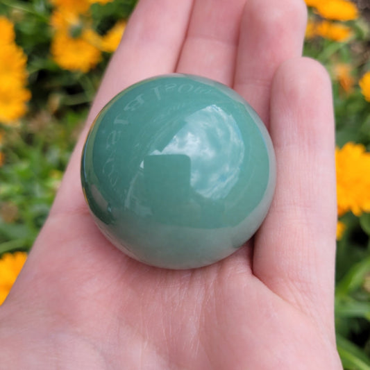 Hand holding polished green aventurine sphere with blurred yellow flowers background
