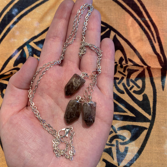Silver chain necklace with three dark stone pendants held in hand against patterned fabric background
