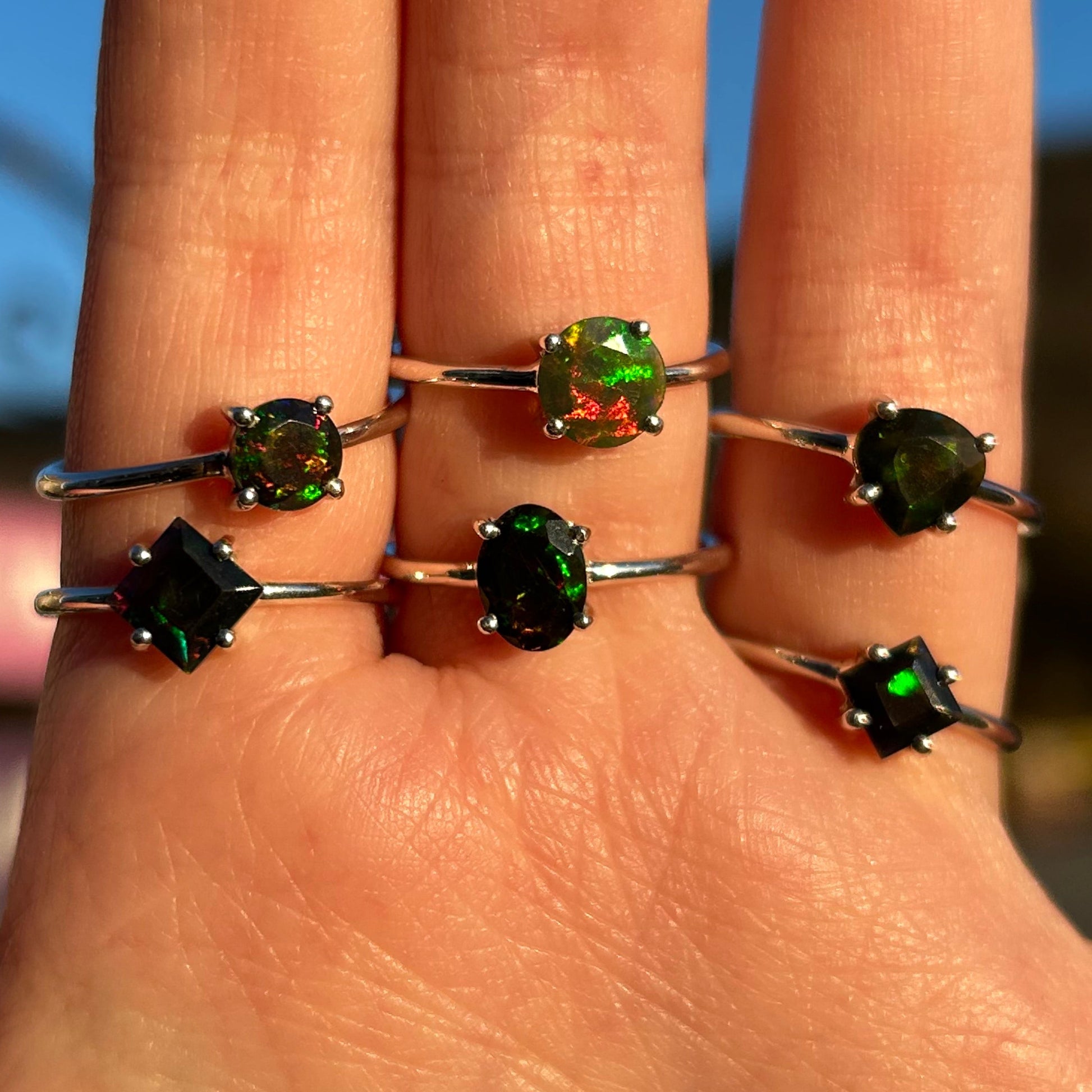 Close-up of hand wearing six *Ringg Black Opal rings with vibrant green and red flashes on silver bands